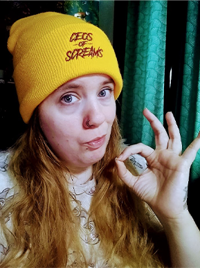A picture of Mareike in a yellow beanie gesturing the ok sign